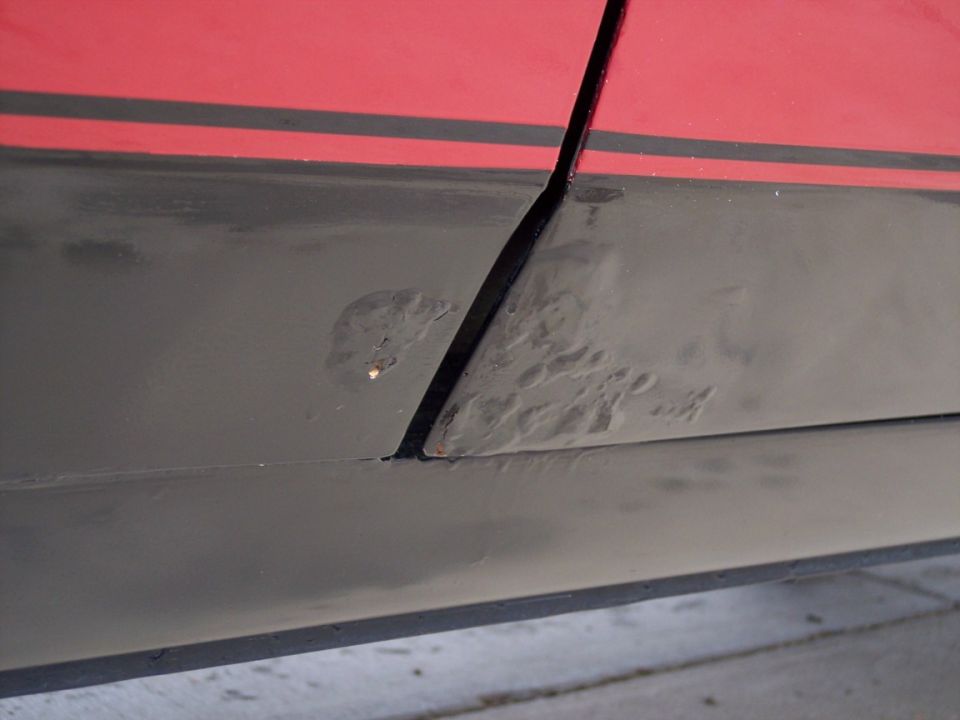 close-up of rust bubbles forming under paint on a car's lower body panel