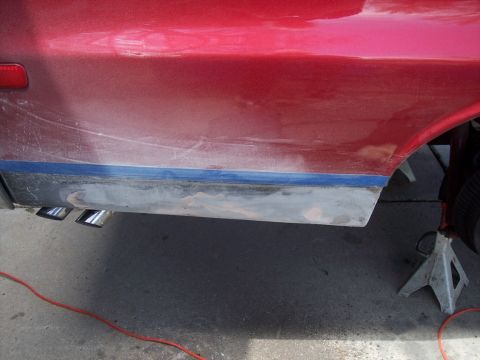 1972 Ford Ranchero - The side panel of a red 1972 Ford Ranchero shows areas of repair and masking tape, with dual exhaust pipes visible.