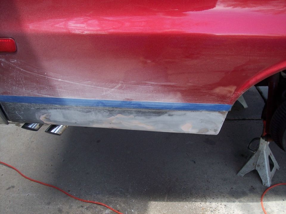 Red quarter panel with rocker ground to bare metal and body filler, blue masking line