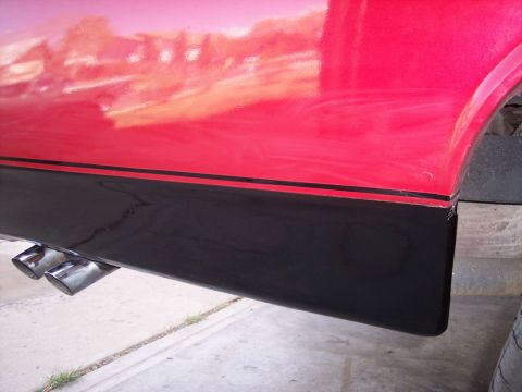 1972 Ford Ranchero - Close-up of the side of a red vehicle, showing black lower body trim and dual exhaust pipes.