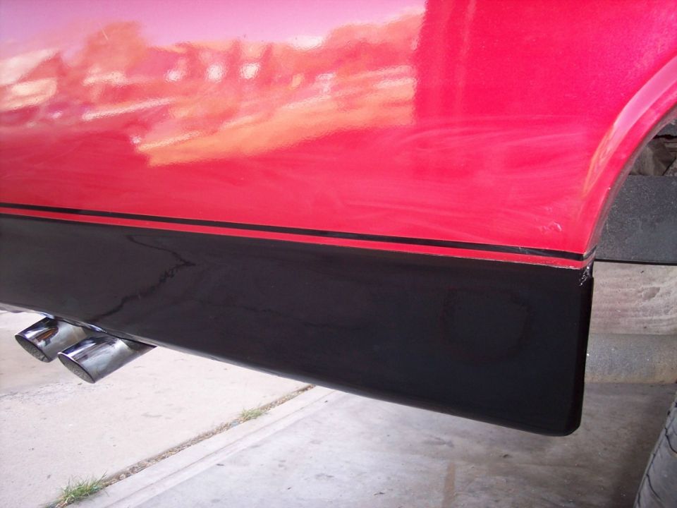 Lower side of a red vehicle with black two-tone panel and dual chrome exhaust tips