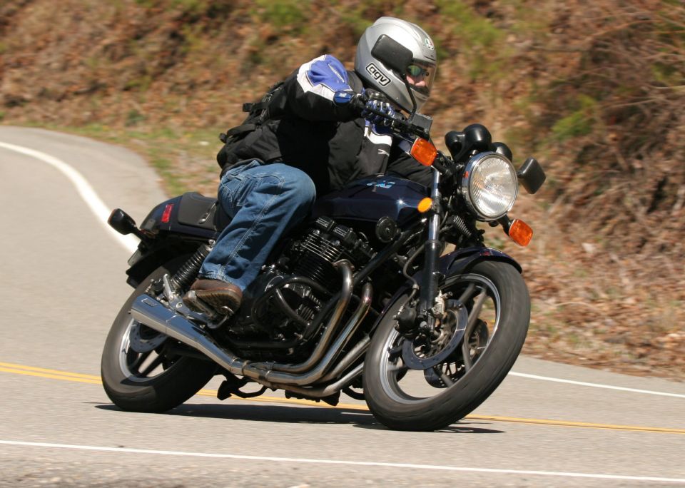 Rider leaning a dark blue inline-four motorcycle through a curve on a country road