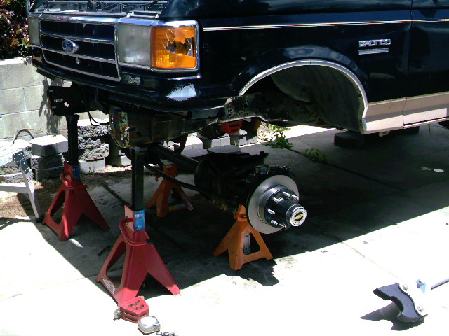 Dark blue Ford 4x4 front end on red jack stands, brake rotor and hub off in a driveway