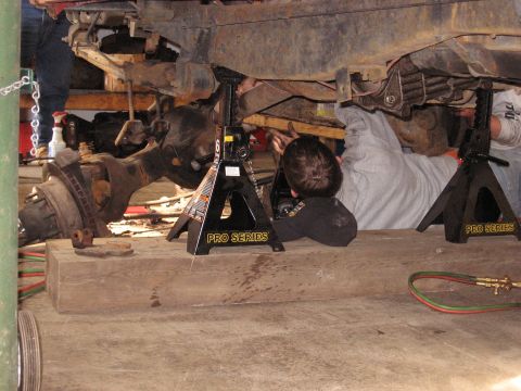 1977 Ford F-150 - Mechanics work on the undercarriage of a vehicle supported by jack stands in a garage.