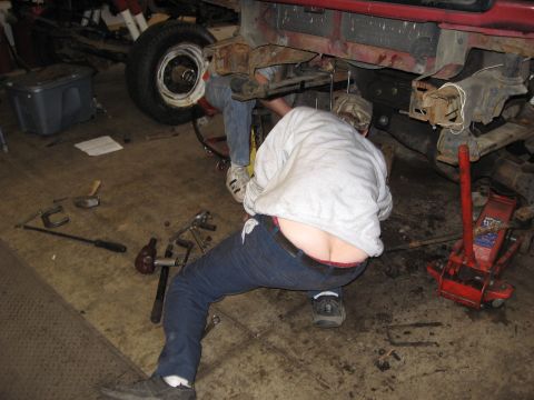 1977 Ford F-150 - A person is working on the underside of a vehicle in a garage setting with tools scattered around.