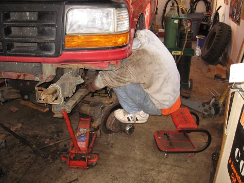 1977 Ford F-150 - A person works on the front suspension of a red Ford truck in a garage setting.