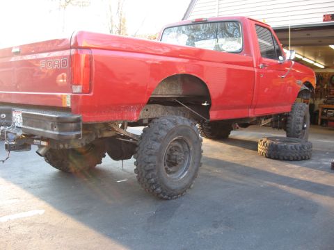 1977 Ford F-150 - Red Ford pickup truck with lifted suspension and large tires, parked in a garage.