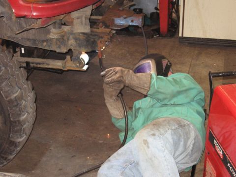 1977 Ford F-150 - A person is welding a part of a vehicle's frame in a garage setting.