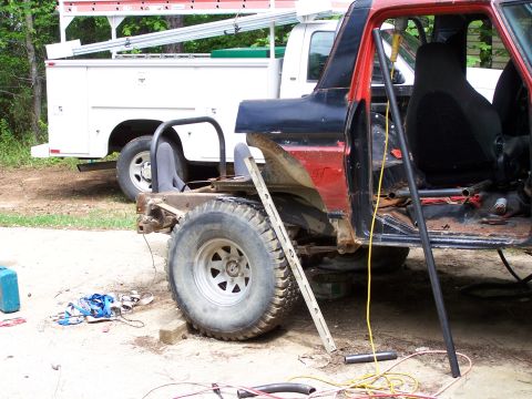 1979 Ford F-150 - A heavily modified 1979 Ford F-150 pickup truck sits in a yard next to a white service truck, undergoing extensive repairs or customization.