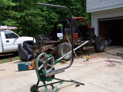 1979 Ford F-150 - A custom vehicle build is underway, a roll cage and a pipe bender, with a white pickup truck parked beside it.