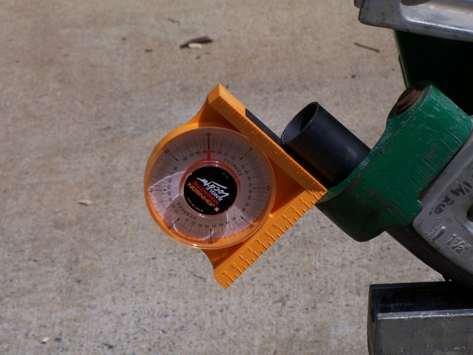 Orange angle locator with black needle on a metal pipe, set against a concrete surface