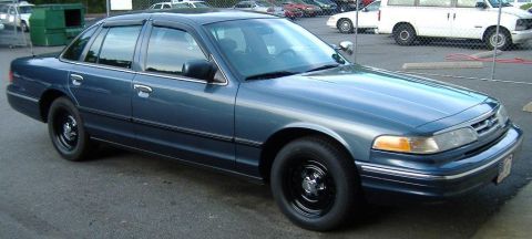 1996 Ford Crown Victoria - A blue sedan is parked in a lot with other vehicles visible in the background.