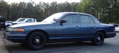 1996 Ford Crown Victoria - A blue 1996 Ford Crown Victoria is parked outdoors with other vehicles in the background.