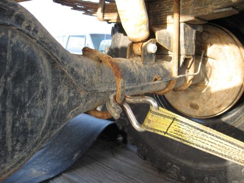 1977 Ford F-150 - Close-up view of a vehicle's rear axle and suspension system, secured with a yellow tie-down strap.