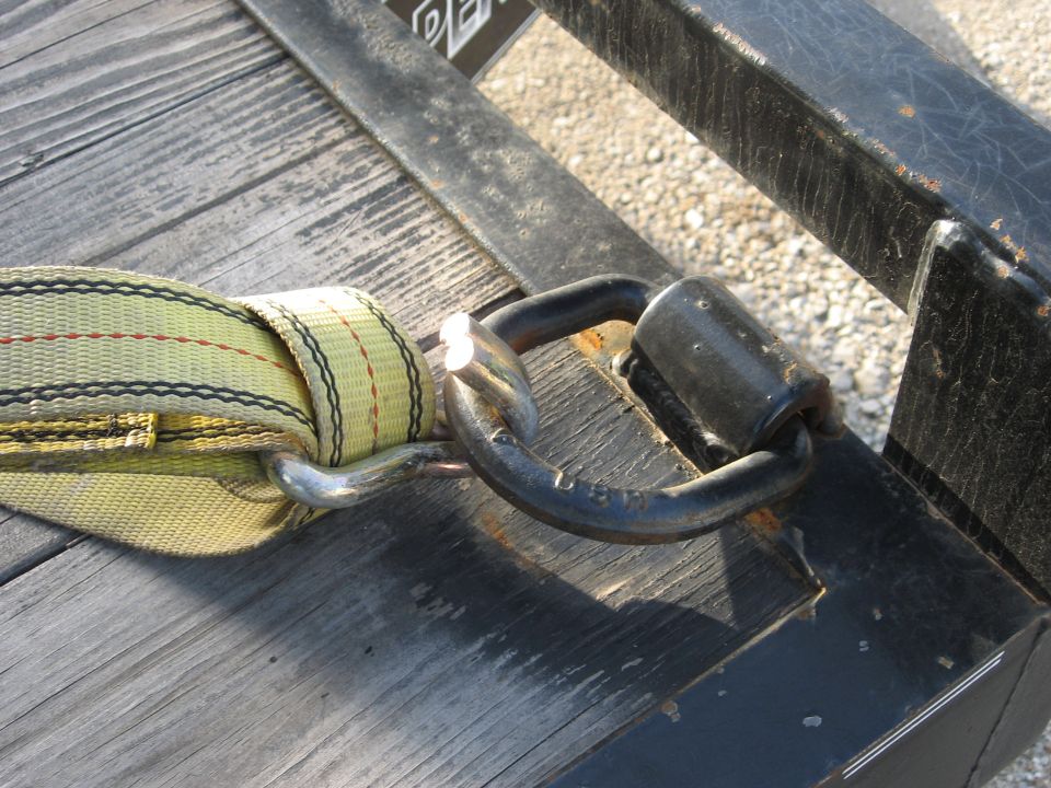 Yellow tie-down strap connected to a black metal D-ring on a wooden trailer deck