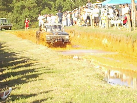 1978 Ford Bronco - A 1978 Ford Bronco navigates a muddy track during an off-road event, with a crowd watching.