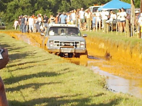 1978 Ford Bronco - A pickup truck powers through a muddy track during an event, with a crowd gathered to watch the action.