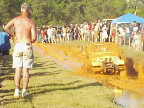 1978 Ford Bronco - A crowd watches as a yellow jeep navigates a challenging mud obstacle course.