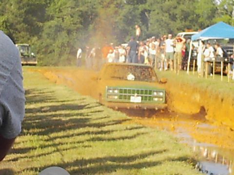 1978 Ford Bronco - A green pickup truck navigates a muddy track with spectators watching.