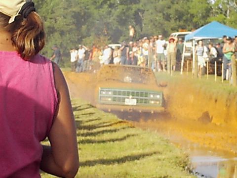 1978 Ford Bronco - A green truck navigates a muddy track with a crowd of onlookers gathered to watch the event.