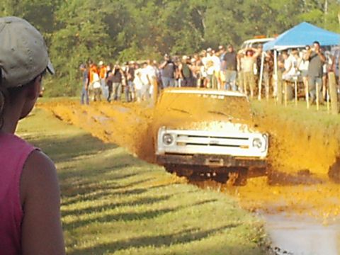 1978 Ford Bronco - A white truck is stuck in a mud pit during an event, with spectators gathered around.