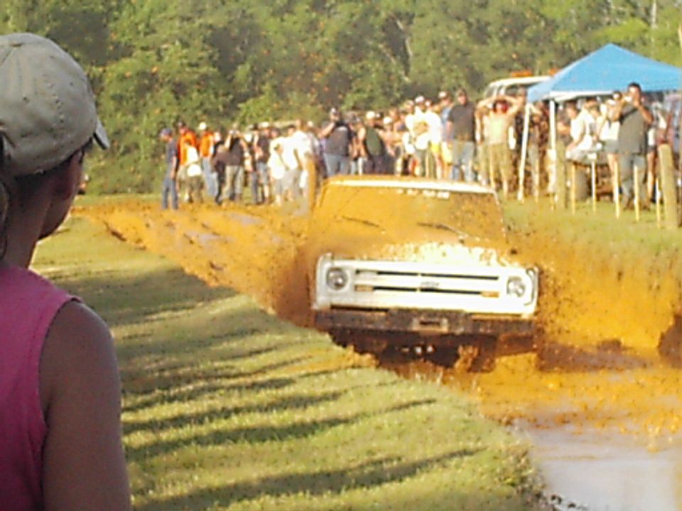 White truck stuck in mud pit with crowd watching