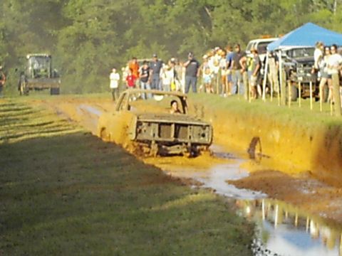 1978 Ford Bronco - A truck navigates a muddy course during a competition, with onlookers gathered to observe the event.