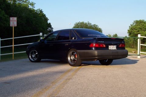 1993 Ford Taurus - Rear view of a dark blue sedan with a spoiler and custom wheels.