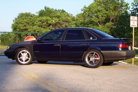 1993 Ford Taurus - A dark blue sedan with aftermarket wheels and red brake calipers is parked on a street.