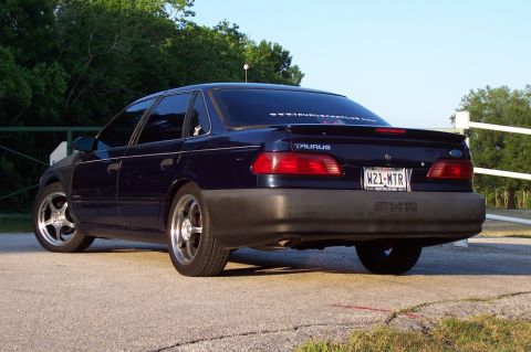 1993 Ford Taurus - Rear view of a dark blue 1993 Ford Taurus sedan, custom wheels and a spoiler.