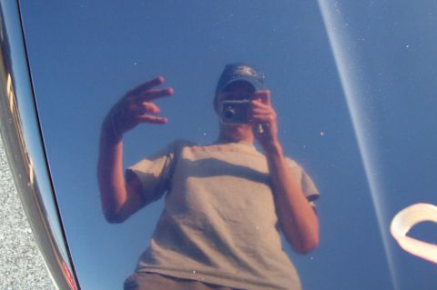 1993 Ford Taurus - Reflection of a person in a car's hood, holding a camera and making a peace sign.