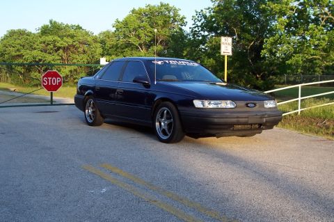 1993 Ford Taurus - Dark blue sedan parked near a gate with a stop sign. The car has aftermarket wheels.