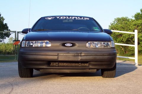1993 Ford Taurus - The front of a dark blue Ford Taurus is shown, a banner on the windshield and a black bumper.