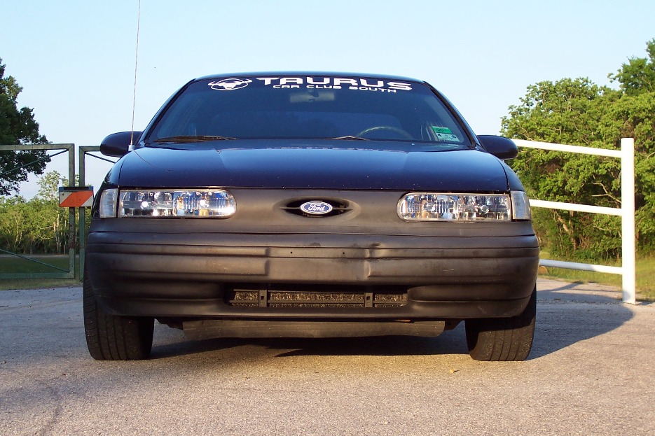 Front view of a dark blue Ford Taurus with a 'Taurus Car Club South' banner on the windshield. It has a black bumper and grille