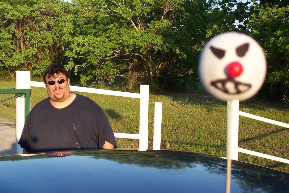 Man standing next to a car with a clown-faced lollipop in the foreground