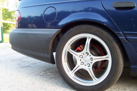 1993 Ford Taurus - The rear quarter panel of a blue 1993 Ford Taurus sedan is shown with custom wheels and red brake calipers.