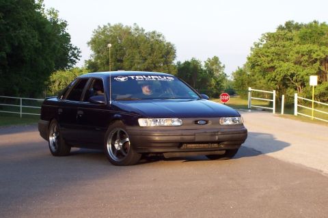 1993 Ford Taurus - A dark blue sedan, identified by a windshield banner as a Taurus, is seen from a 3/4 front angle on a road.