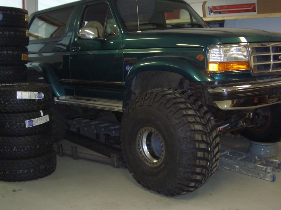 Dark green lifted Ford Bronco SUV on huge mud tires in a garage