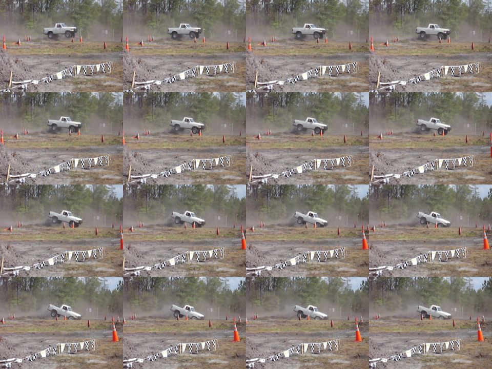 White pickup truck driving on a dirt track with orange cones and checkered flags