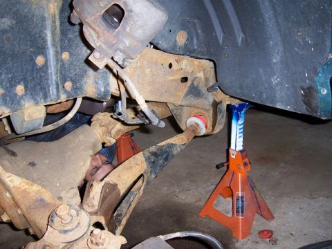 1996 Ford Bronco - A person works on the rusty suspension of a vehicle supported by jack stands.