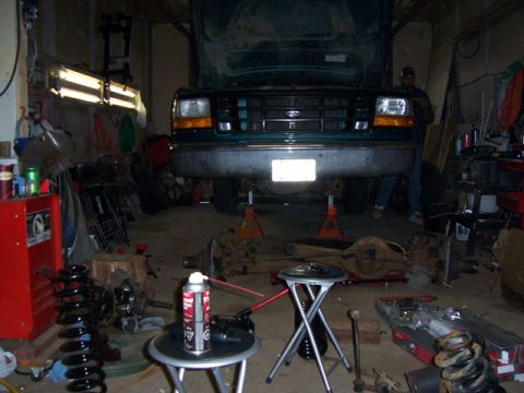 1996 Ford Bronco - A green 1996 Ford Bronco is shown on jack stands in a garage, with its hood open and parts scattered around.
