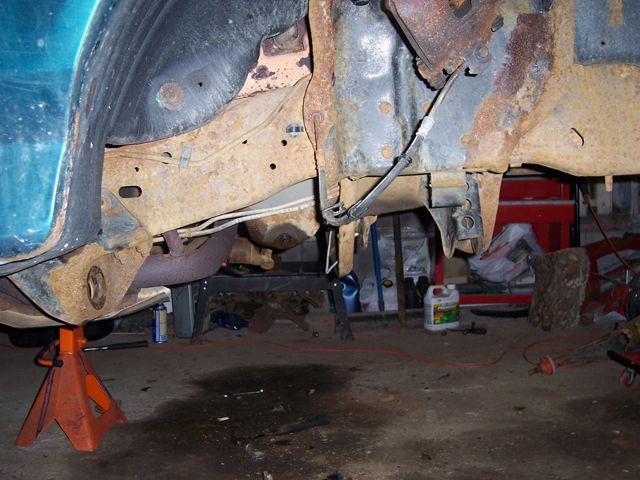 Underside of green truck front frame rail with suspension removed, on an orange jack stand