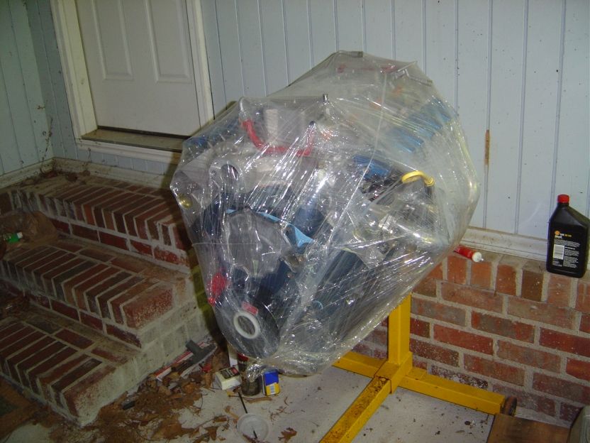 Blue V8 engine wrapped in plastic on a yellow engine stand in a garage