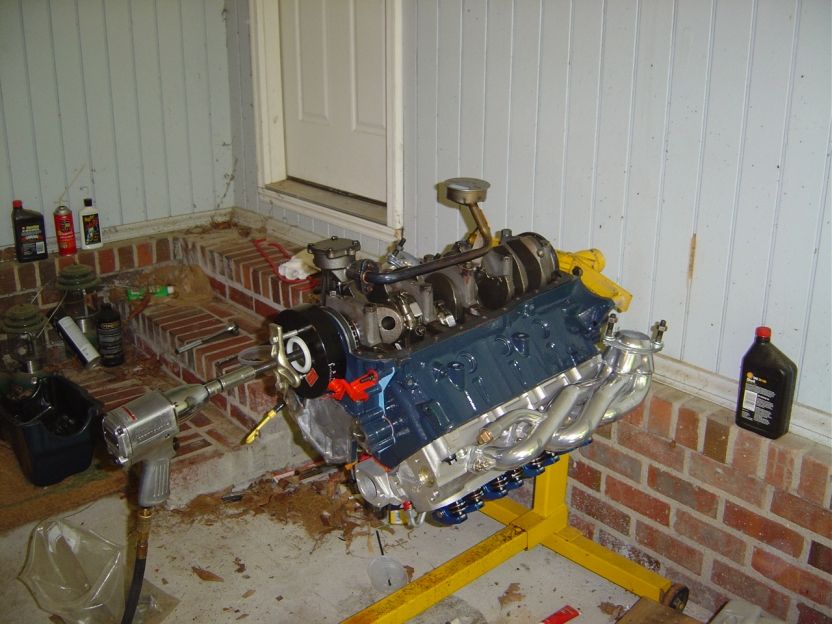 Blue Ford V8 engine on a yellow stand mid-build with polished shorty headers
