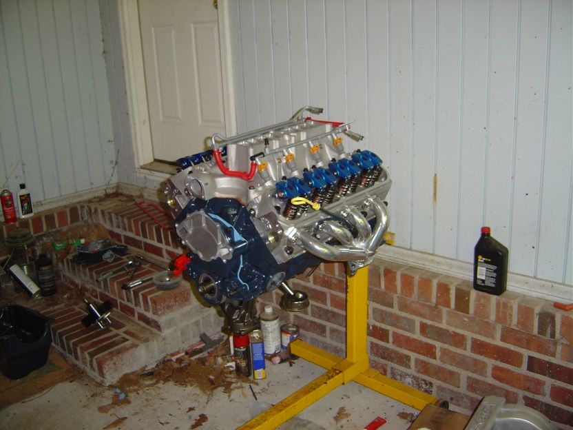 Fresh Ford V8 on a yellow engine stand with headers and blue valve springs