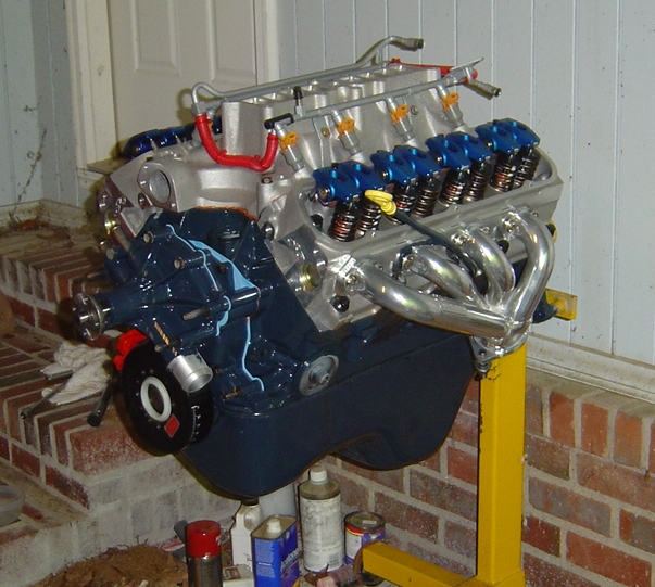 V8 engine on yellow stand with aluminum heads, chrome headers, valve covers off