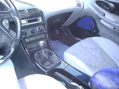 1995 Ford Probe - Interior view of a car's dashboard, center console with manual shifter, and patterned seats. Text "SUPERMOTORS.NET" is visible.