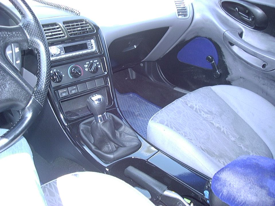 Car interior with manual shifter, dashboard, and patterned seats. "SUPERMOTORS.NET" visible