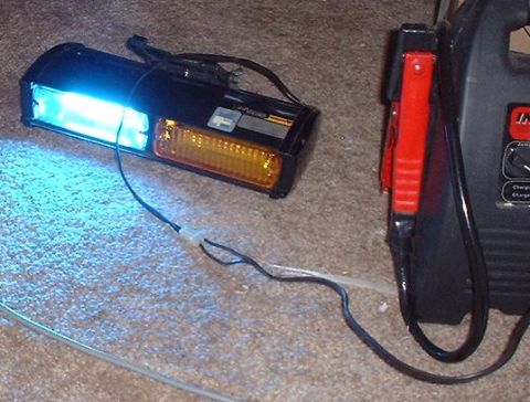 1997 Ford Crown Victoria - A car headlight assembly with blue and amber lights is connected to jumper cables, with a battery charger visible on the right.
