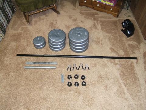 1998 Ford Taurus - Weight plates, barbell, and collars are laid out on a carpeted floor, likely for a home gym setup.